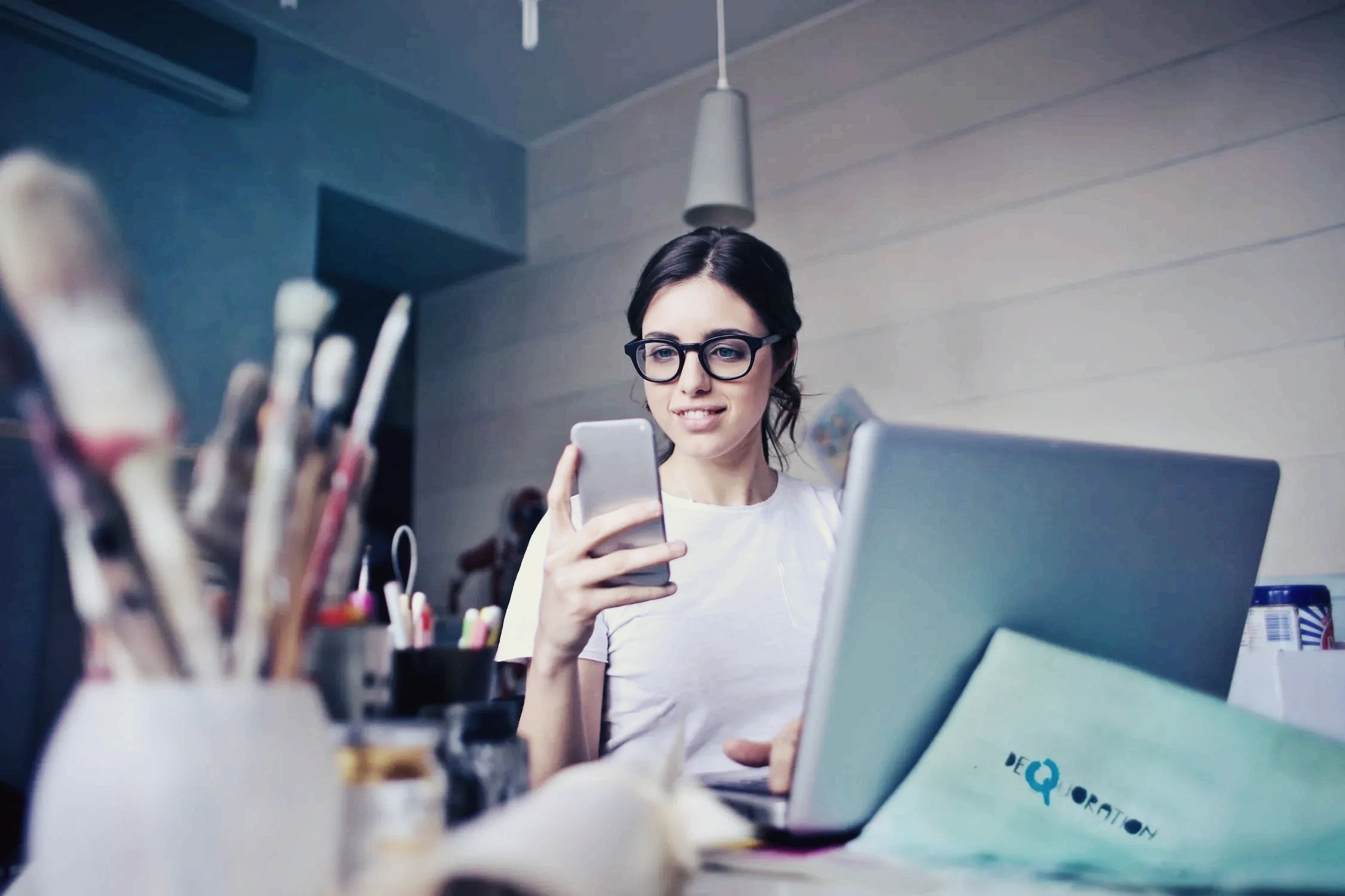 A founder working at a laptop while glancing at her phone in warm natural light