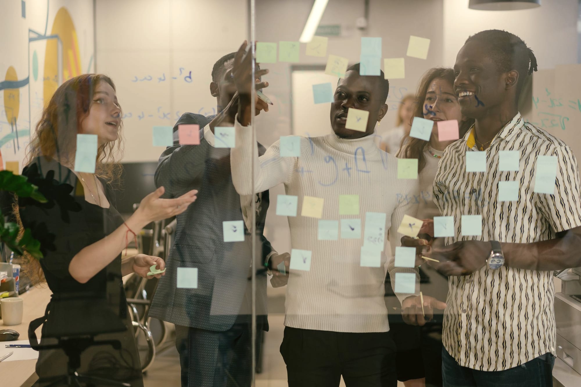 Colleagues working through sticky notes on a glass wall in a bright office.