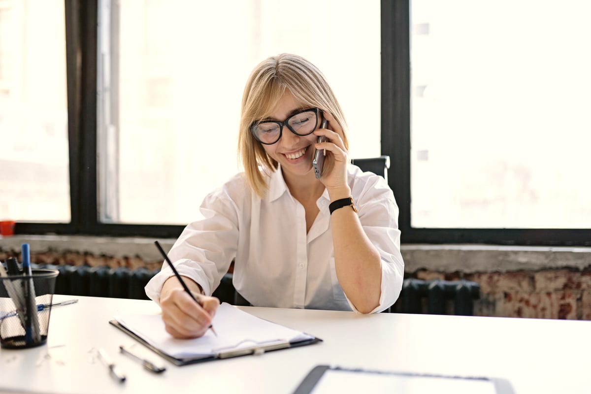 A candidate smiling on a phone call while taking notes at a bright desk.
